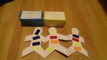Multi-coloured stickers on back of paper chain people and a yellow and blue box of 'medicine'